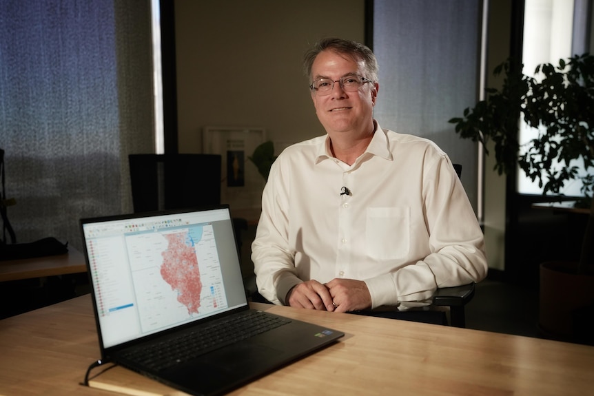 A man poses at a desk with a map on a laptop