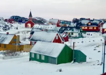 BBC A town in typical Greenland style is pictured - brightly-painted wooden walls and triangular roofs covered in snow are the main features of these sparsely dotted homes