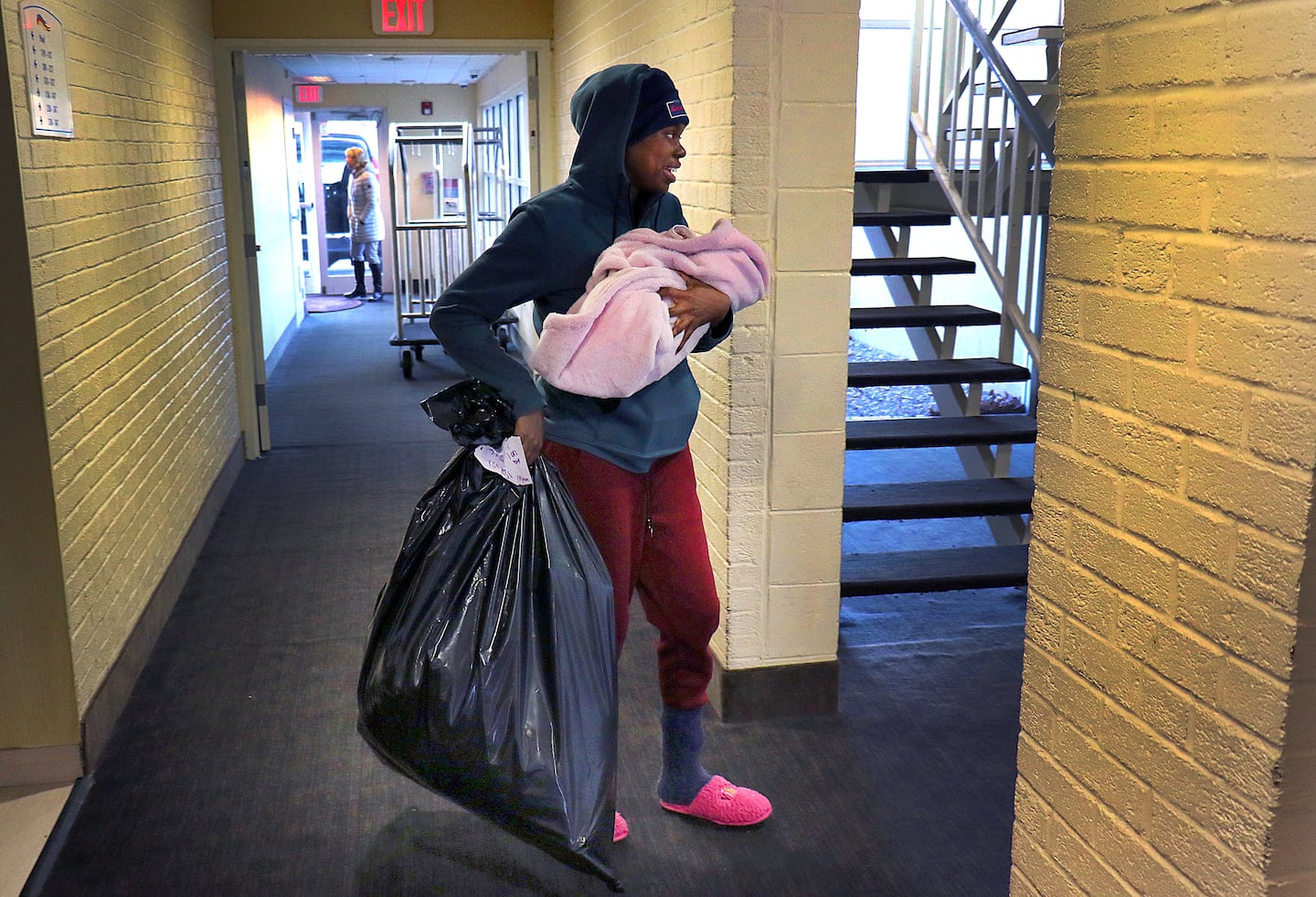 Haitian migrant Jolaine held her 20-day-old baby, Hadasa, as she carried a bag of donated clothing to her room before a holiday party hosted by the Plymouth Area Coalition for the Homeless for migrants being housed at the Baymont Inn in Kingston in 2022. 