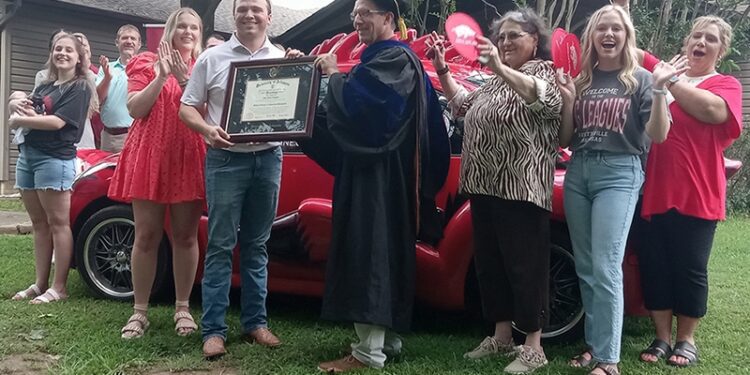 Tyler Huggins, center left, accepts his diploma from Kerry Melton of the College of Engineering while his wife, Anna, to his right, celebrates with other family members in Bono on June 26.