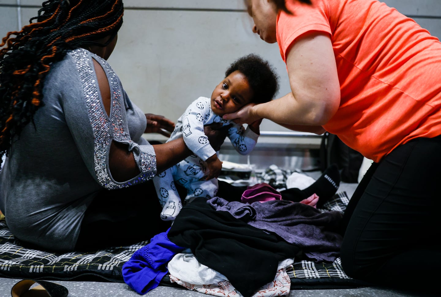 Sherlie Elisse (left) held her baby, Elisonn Saint Juste, while Sarah Hoff, a volunteer helping families at Logan Airport, checked his clothing size while distributing donations at the airport in July.