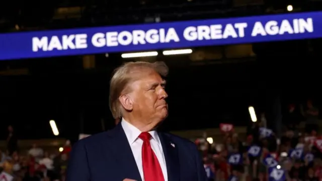 Trump at his rally in Georgia stood under a sign that says