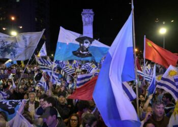 Supporters of parties of the Republican Coalition wave flags as Uruguay's presidential candidate for the Partido Nacional (National Party), Alvaro Delgado (out of frame), speaks during a celebration of the ruling center-right coalition after partial results of the presidential and legislative election were announced, at Plaza Varela Square in Montevideo on October 27, 2024.