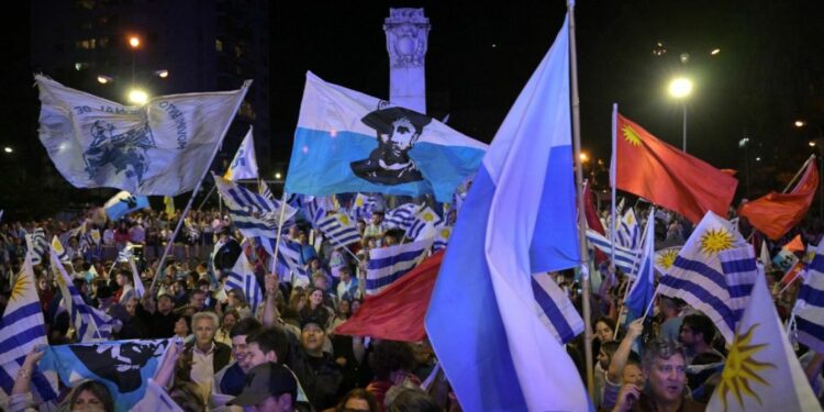 Supporters of parties of the Republican Coalition wave flags as Uruguay's presidential candidate for the Partido Nacional (National Party), Alvaro Delgado (out of frame), speaks during a celebration of the ruling center-right coalition after partial results of the presidential and legislative election were announced, at Plaza Varela Square in Montevideo on October 27, 2024.