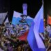 Supporters of parties of the Republican Coalition wave flags as Uruguay's presidential candidate for the Partido Nacional (National Party), Alvaro Delgado (out of frame), speaks during a celebration of the ruling center-right coalition after partial results of the presidential and legislative election were announced, at Plaza Varela Square in Montevideo on October 27, 2024.