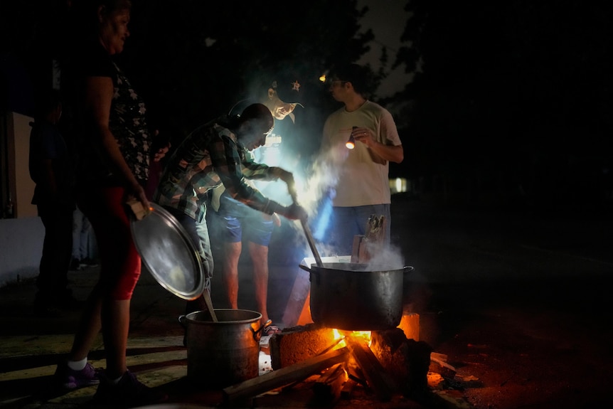 Cuban residents cook over a woodfire stove in the middle of the street in Havana using torches to generate light