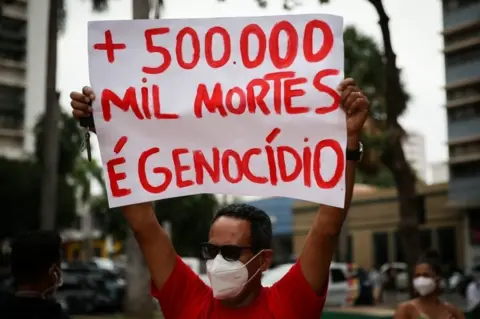 EPA A man holds up a sign protesting against the Covid death toll in Brazil