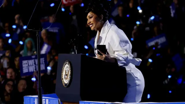 Cardi B stands at a podium in a white dress