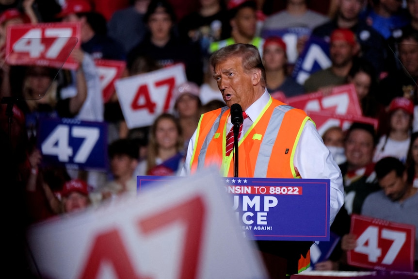 Mid-range shot of Donald Trump at the lecturn wearing an orange vest 