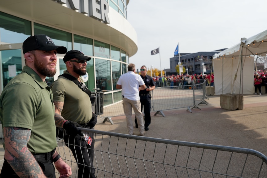 Two burly men watch a crowd enter a stadium 