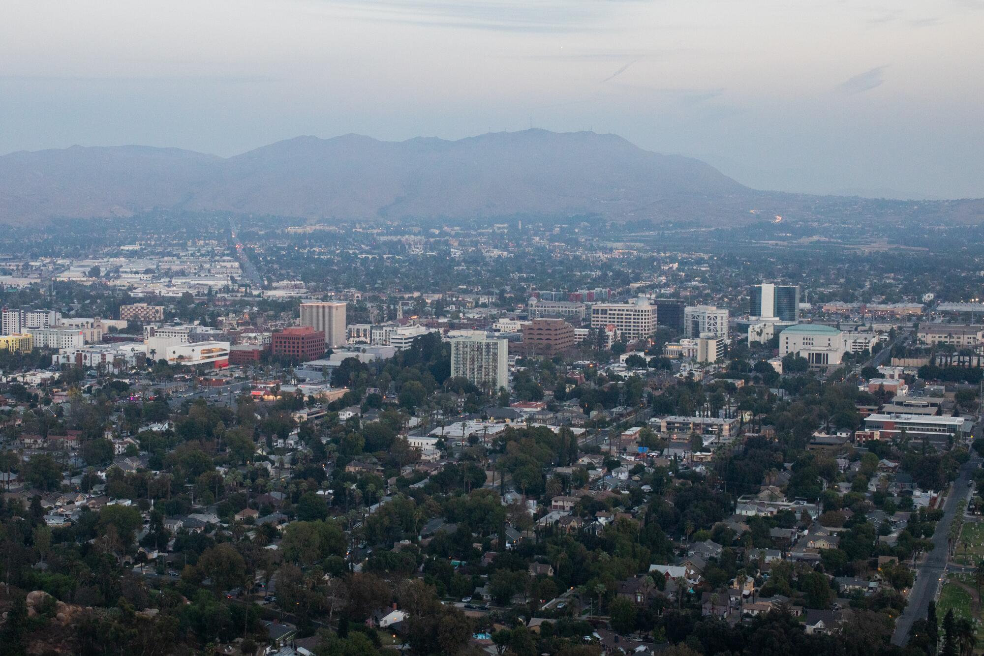 A view from a hilltop toward the buildings of a city beneath hazy skies.