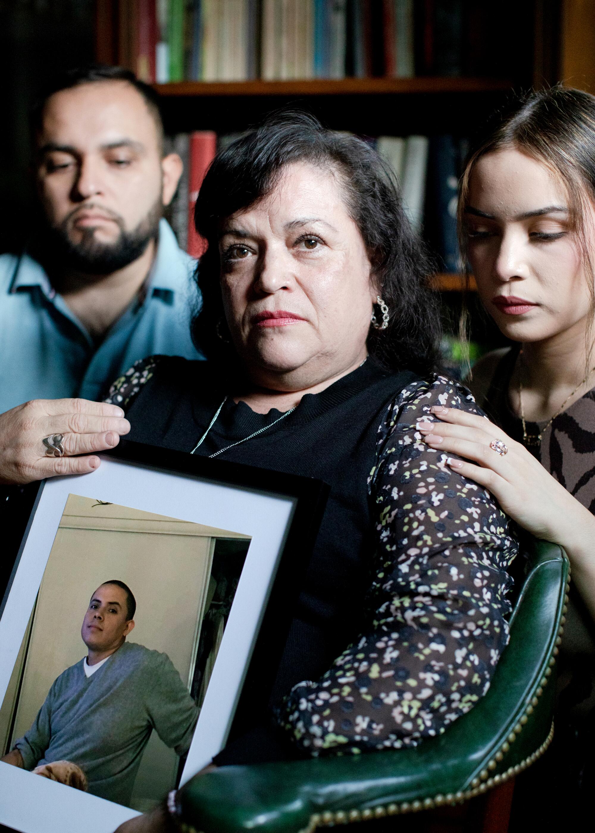 Siblings and their mother sit with a photo of a man.