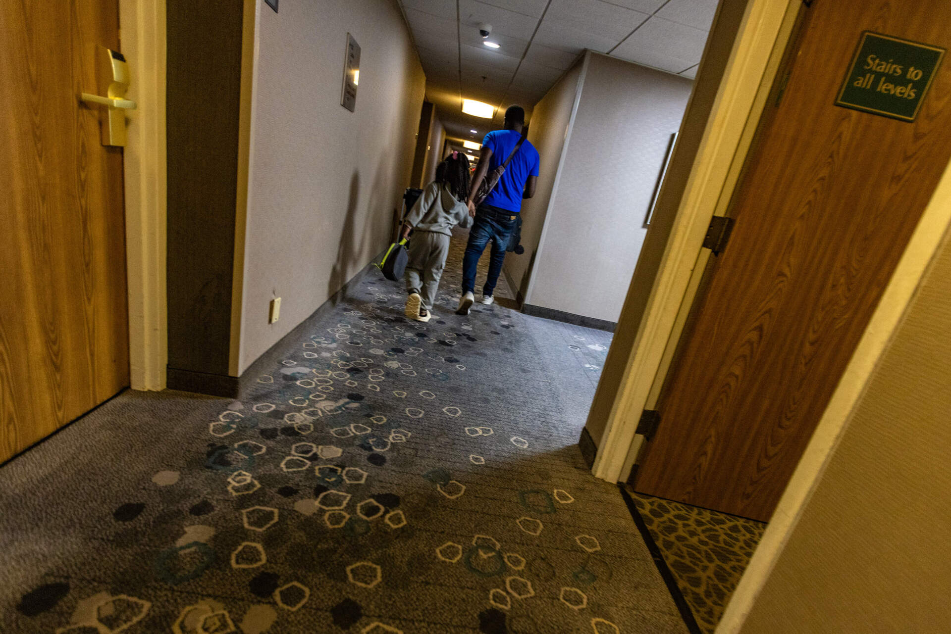 Two migrants walk down the hallway of a Stoughton hotel being used as a shelter for migrants. (Jesse Costa/WBUR)