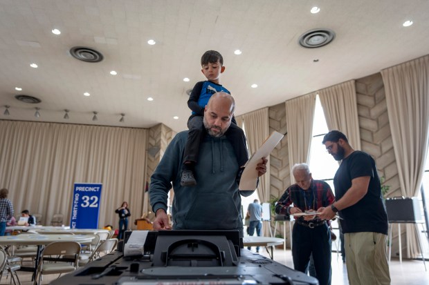 Three-year-old Zayn, sits on his father’s shoulders as he inserts...