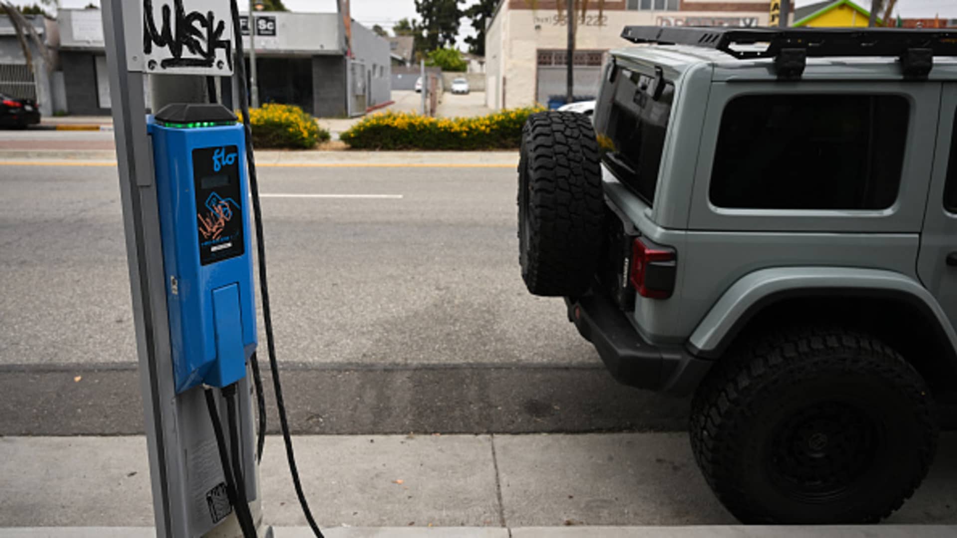 A vandalized FLO public electric vehicle charger sits unused as a Jeep hybrid-electric vehicle sits parked in Los Angeles, California on May 16, 2024. 