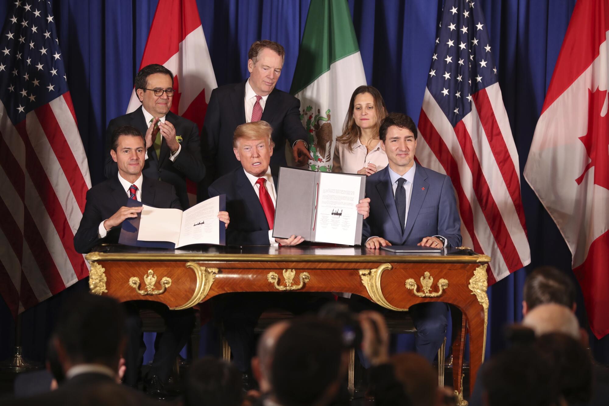 Three politicians sit side-by-side at an ornate table after signing a trade pact.