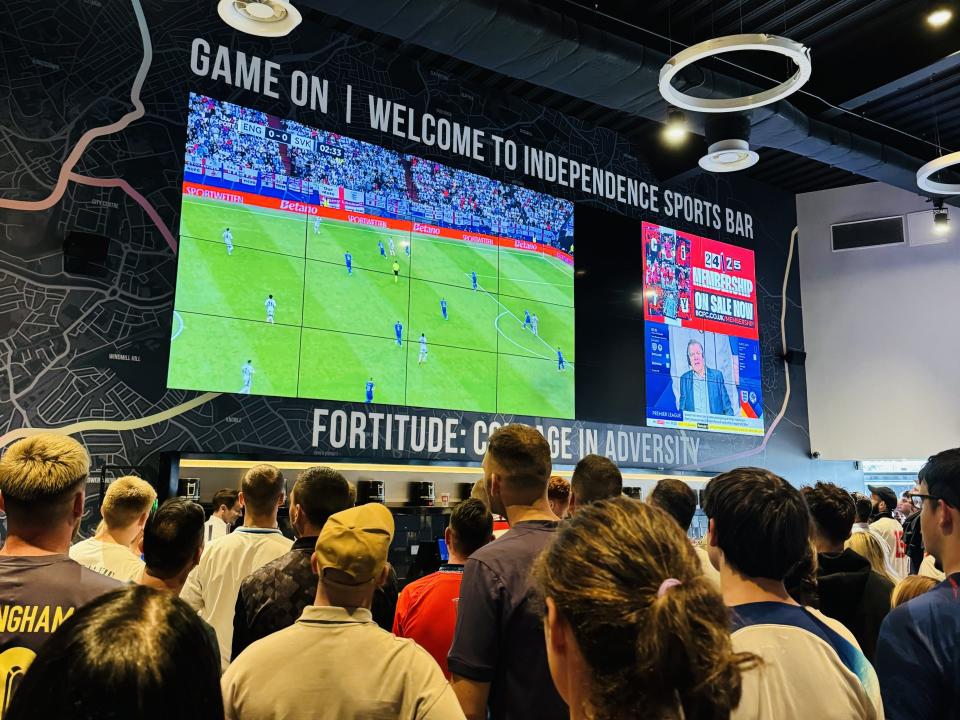 Fans watching a soccer game on a huge screen in a bar.