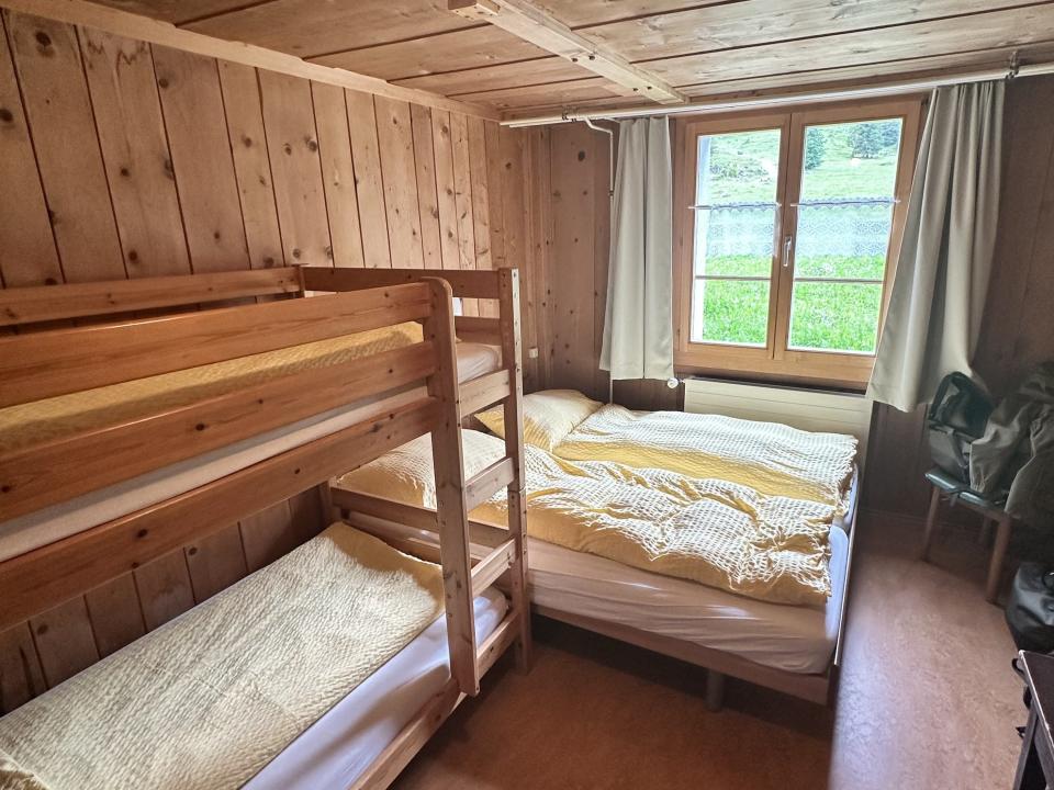 A bed with two duvets next to a bunk bed. There is also a window with green curtains.