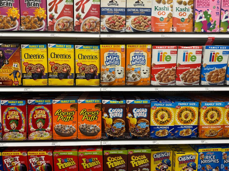 Four grocery-store shelves holding different types of cereal.