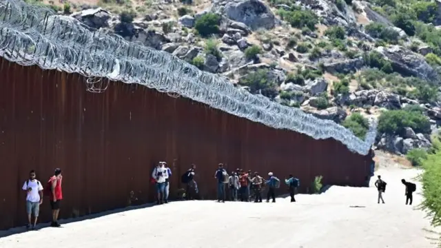 People walking next to the US-Mexico border wall