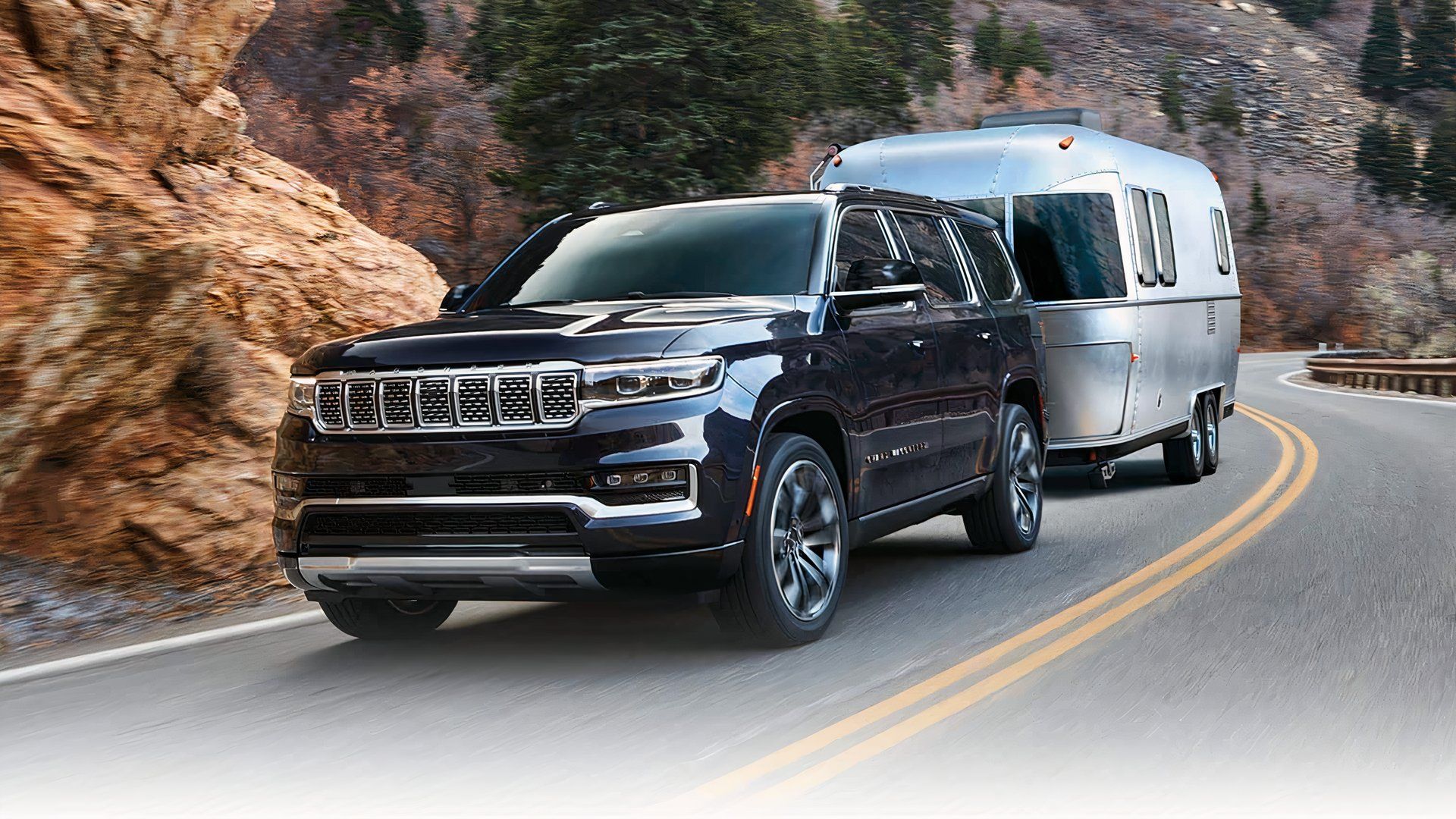 2024 Jeep Grand Wagoneer in black Towing a Travel Trailer along desert road