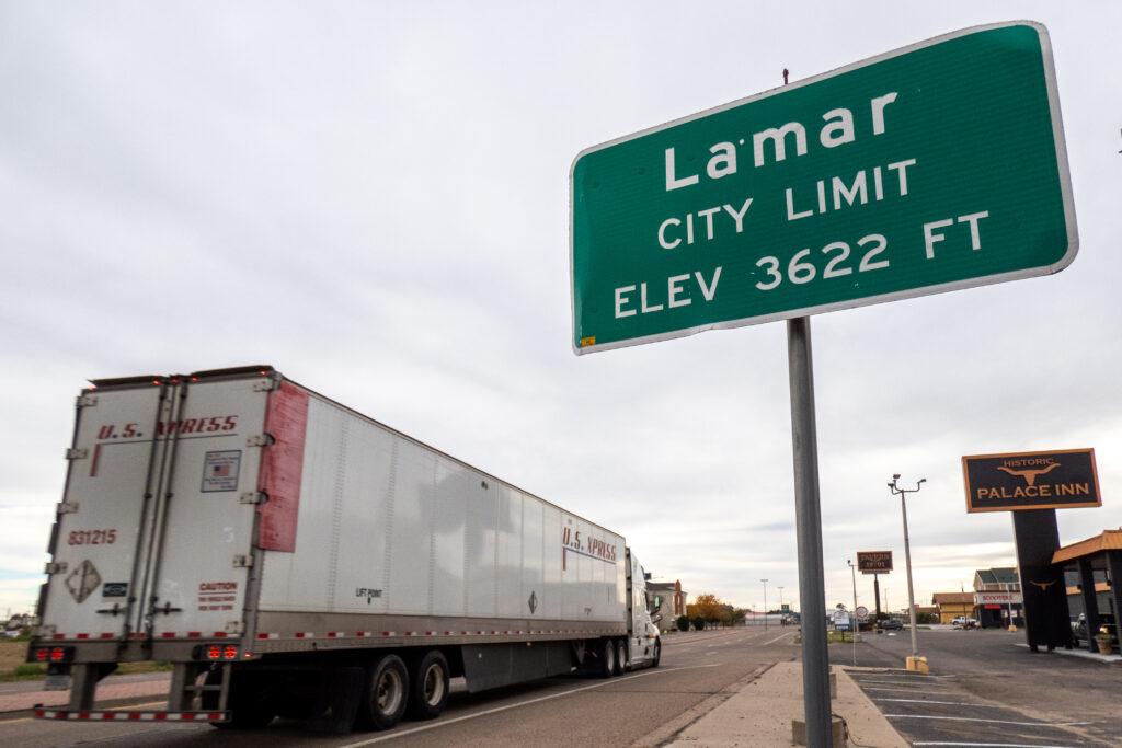 a semi trailer truck passes by a green and white city sign