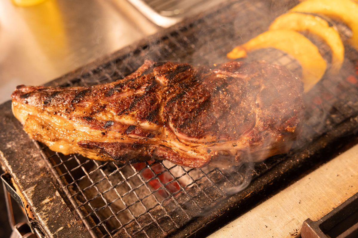 A bone-in steak sears and smokes on a small grill next to rings of acorn squash  