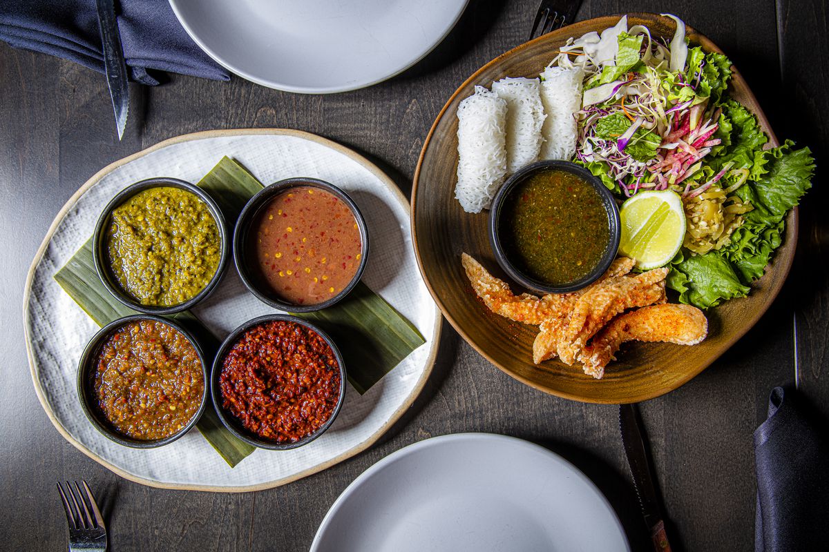 A dish of four colorful hot sauces next to a dish of fried catfish with garnishes.  