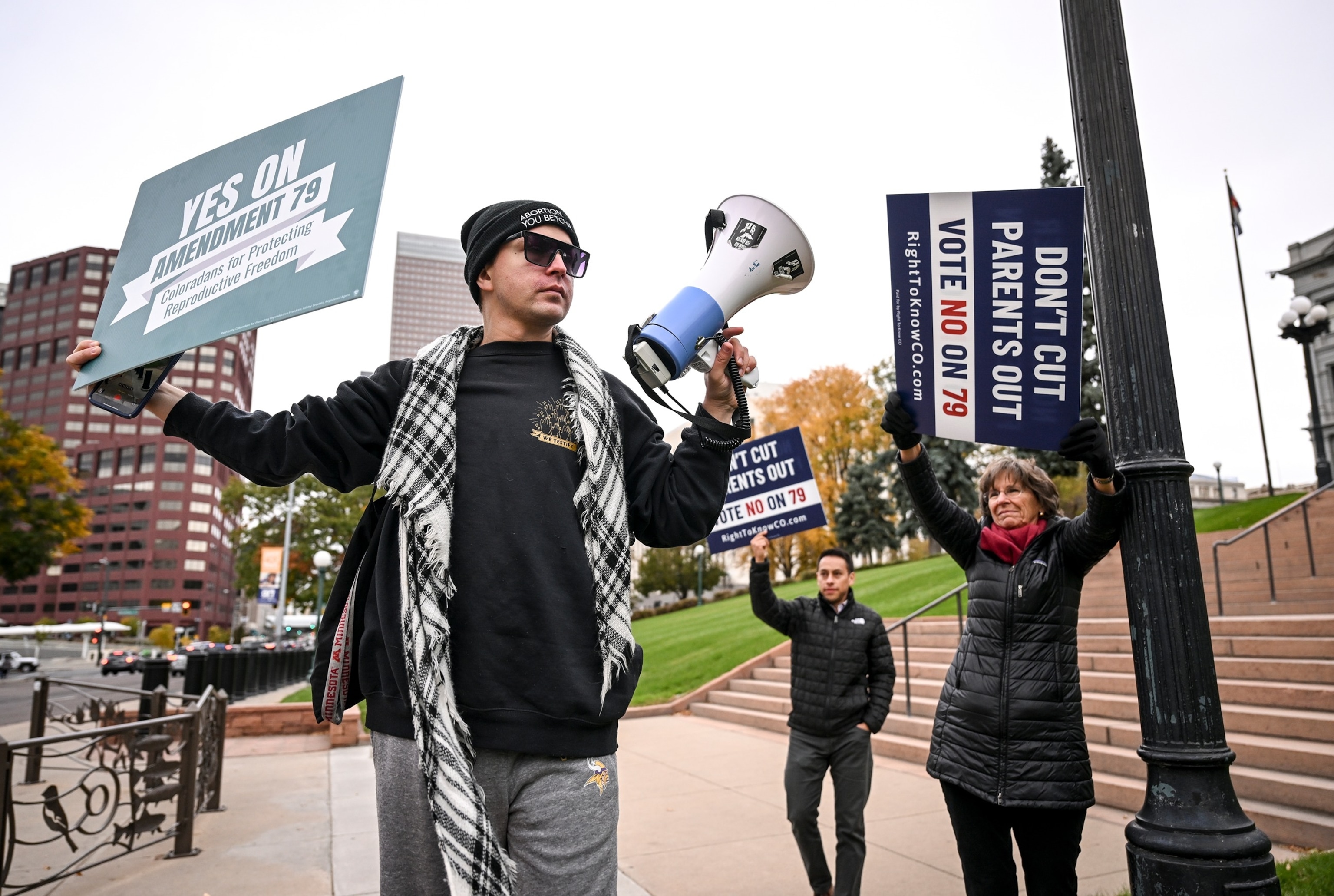 PHOTO: Derek Torstenson makes a pro-choice statement with the use of a bullhorn as Edgar Mares and Susan Gills join others rallying against Amendment 79 at the Colorado State Capitol, Oct. 30, 2024. 