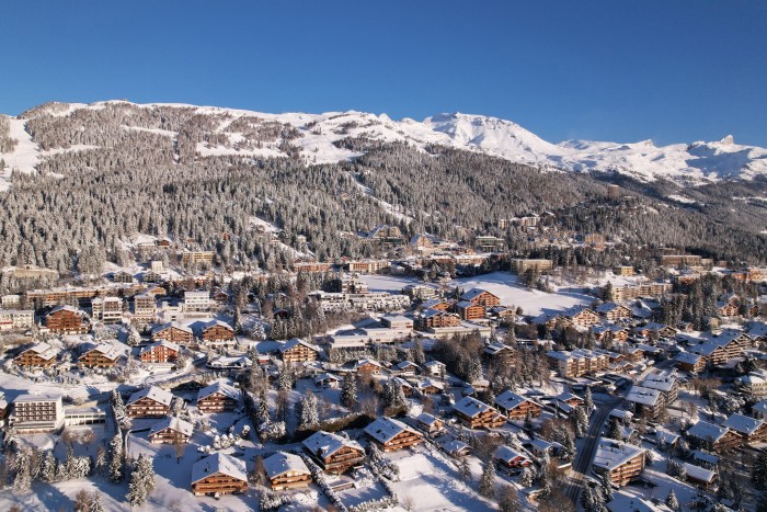 A mountain village nestled among snowy alpine forests. The village consists of traditional wooden chalets and some modern buildings