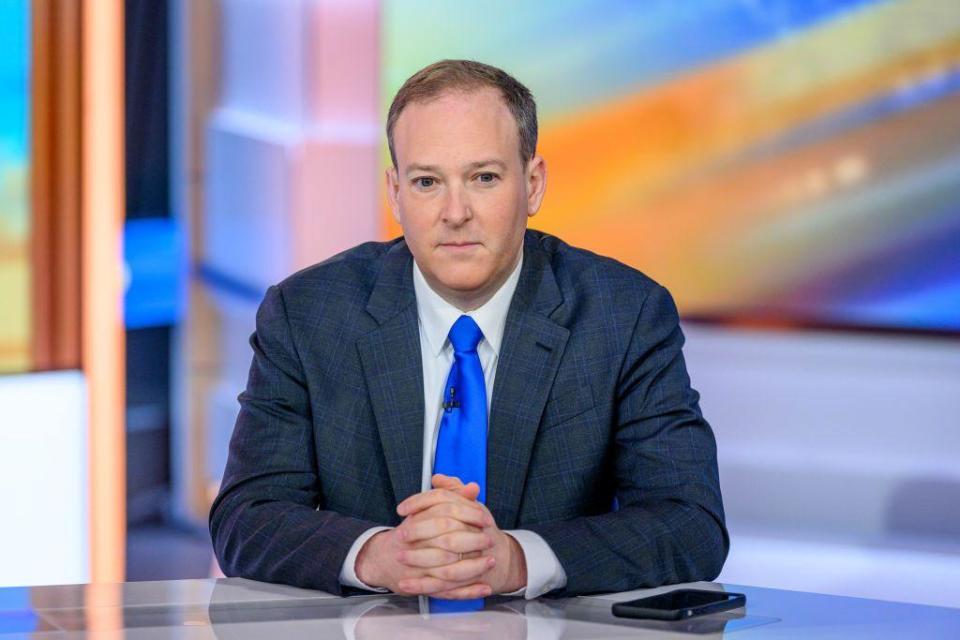 Man sits with his hands folded while wearing a blue tie