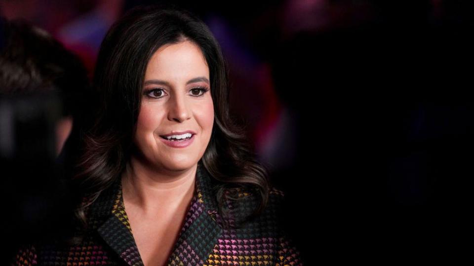 Elise Stefanik, with her black shoulder-length hair down and wearing a multi-coloured suit, speaks with members of the media