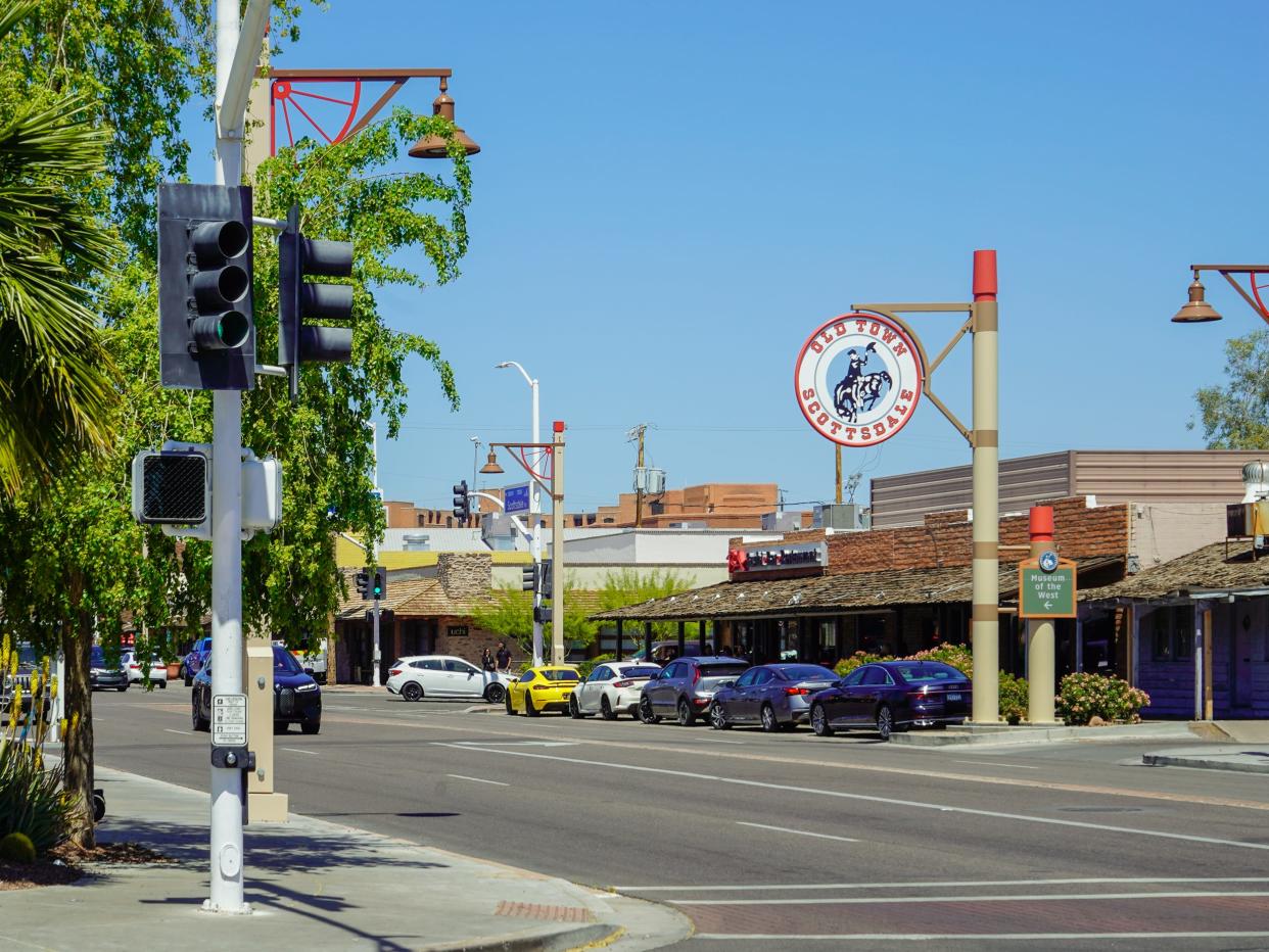 A cross street with trees on the left and buildings on the right on a clear day with blue skies