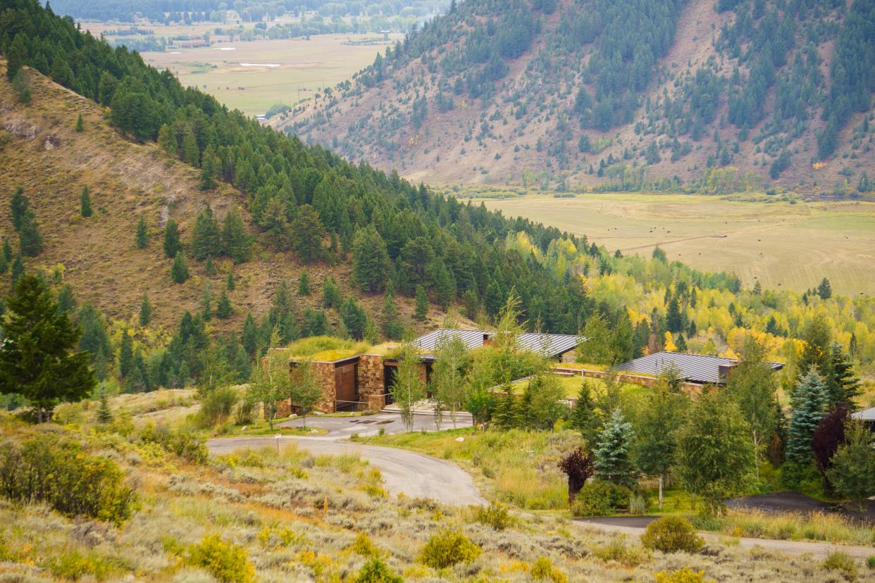 A large, modern home with mountains lined with forests in the background