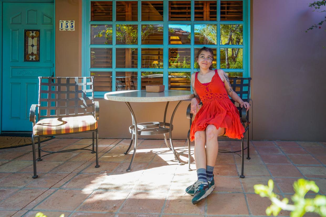 The author sits in a red dress on an adobe patio on a chair next to a table.