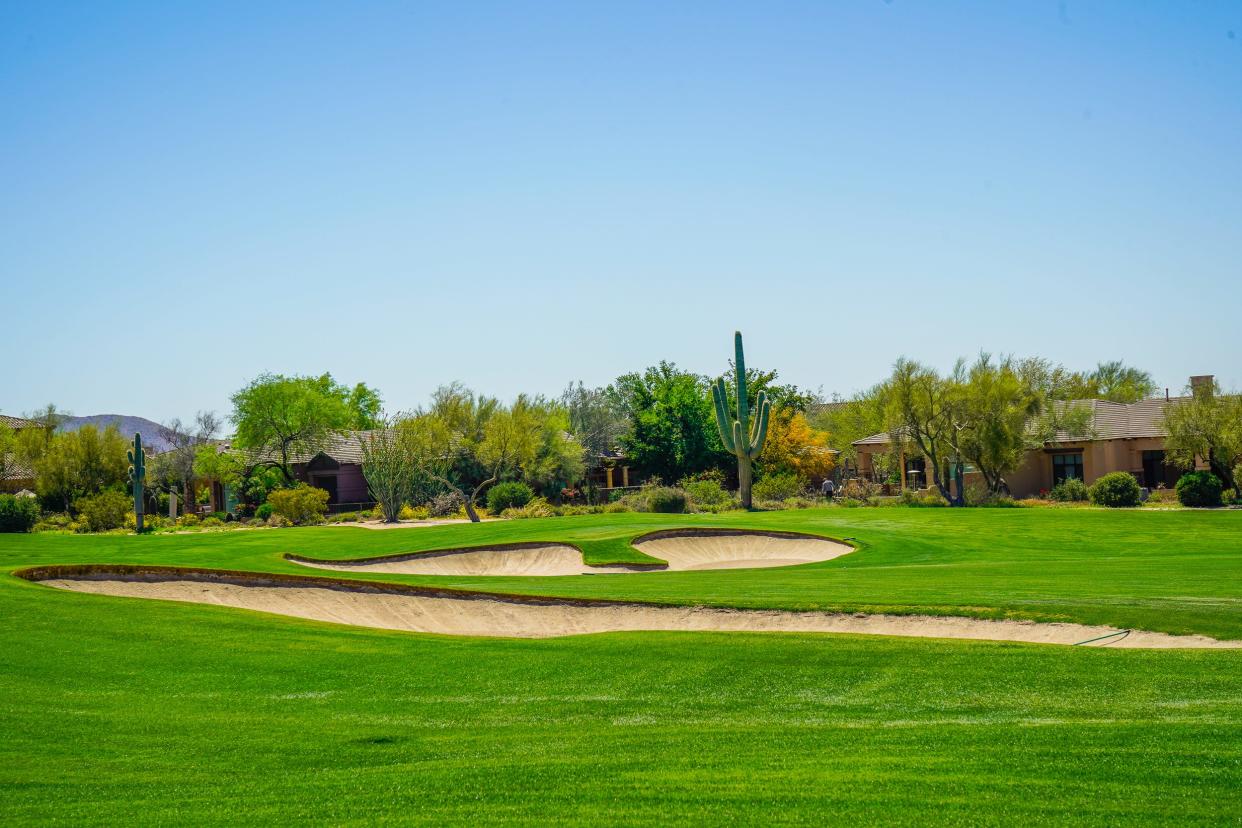 A golf course with sand dunes in front of cacti and homes with blue skies in the background