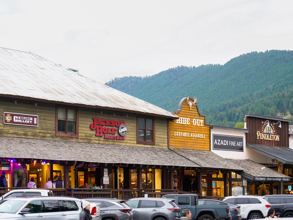 A street full of parked cars in front of a shopping center with a mountain in the background