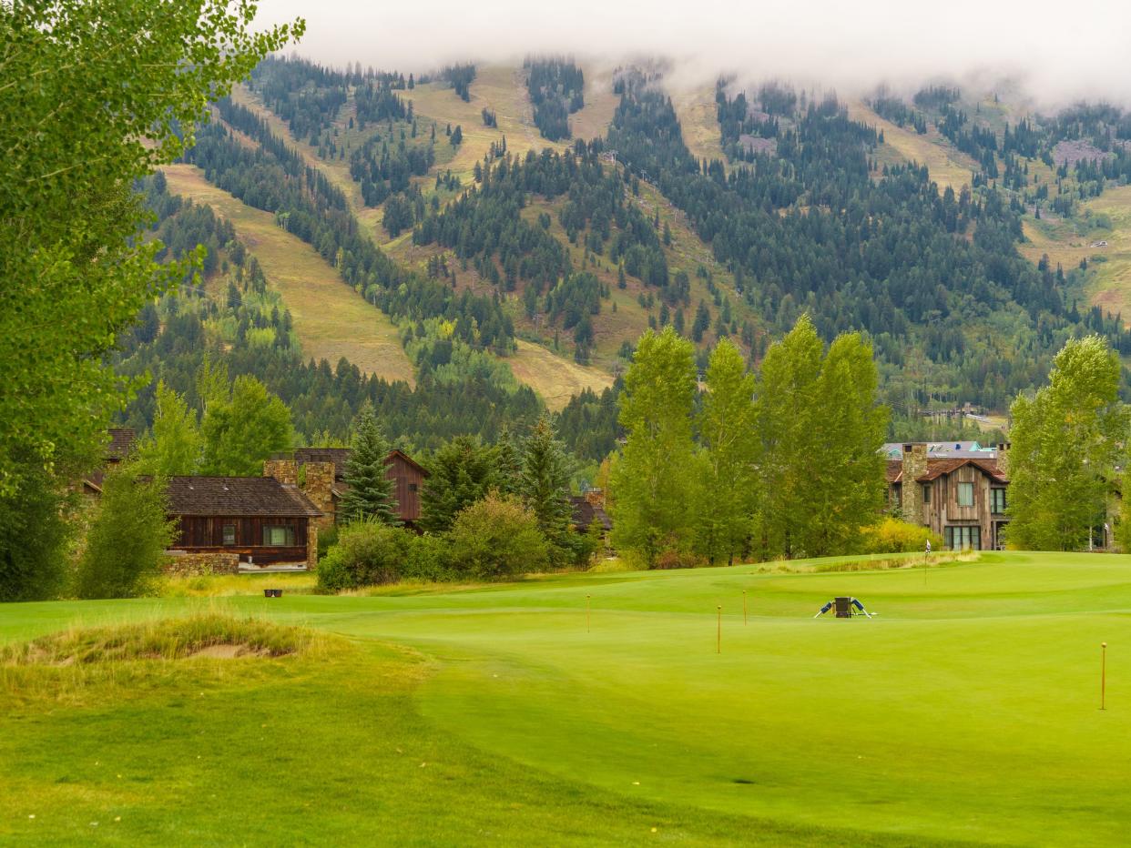 Wood homes behind a golf course with a mountain and a hazy cloud in the background