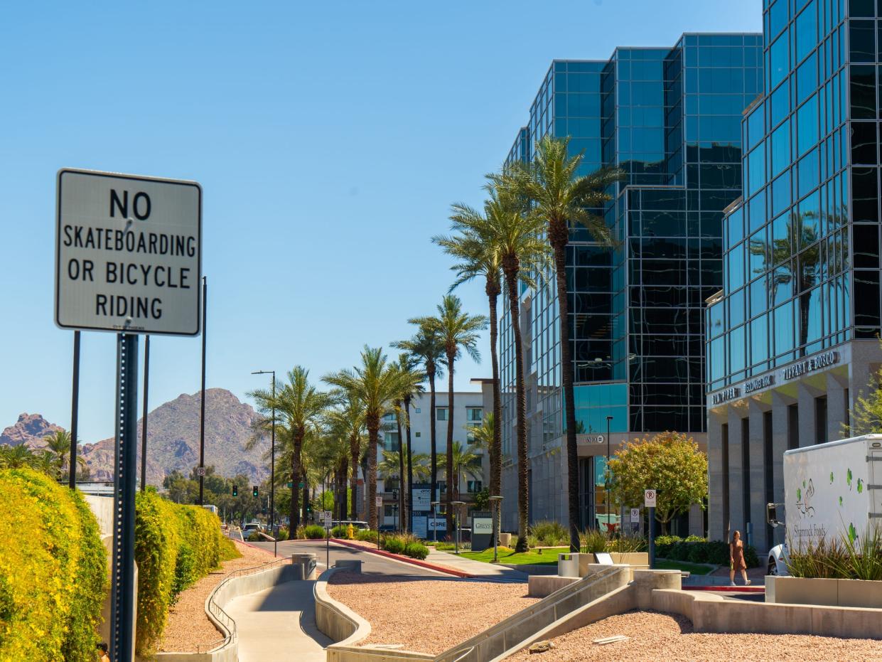 A curvy street in Scottsdale lined with modern buildings and palm trees. Mountains and blue skies in the background