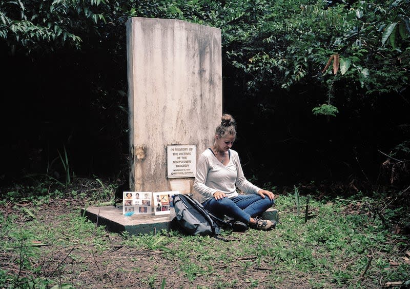 In this March 5, 2018 photo released by Kevin Kunishi, Jordan Vilchez sits at memorial for mass murder and suicide victims at the Jonestown settlement in Guyana. Vilchez returned to Jonestown for the first time in 40 years. (Kevin Kunishi via AP)