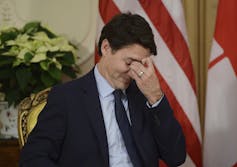 A dark-haired man bows his head with his left hand to his face.