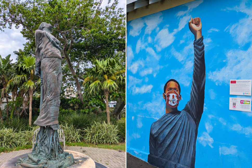 A photo of a bronze statue of a standing figure, roots entangling its feet, surrounded by tropical greenery. Next to it, a colorful mural depicting a person wearing a mask with an arm raised in defiance, set against a sky-blue background with clouds.