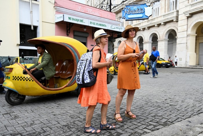 Two tourists stand in front of a three-wheel taxi on a Havana street