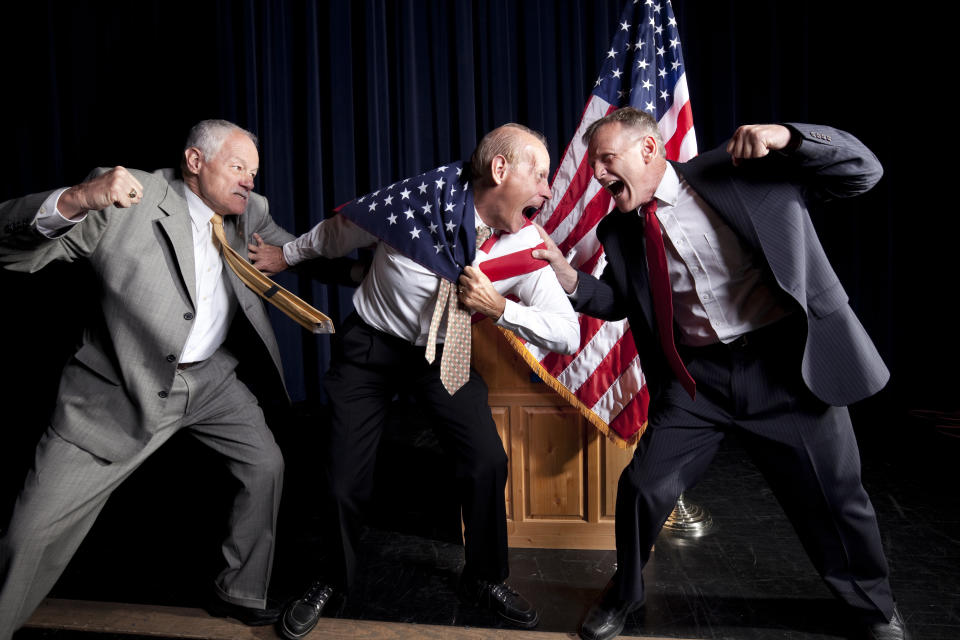 Three men in suits, engaged in a heated argument, pose dramatically with an American flag in the background