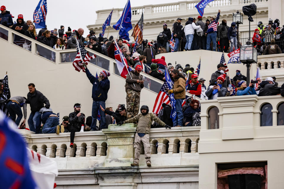 Crowd with flags gathered on building steps during a protest. Some hold American flags; people appear active and engaged