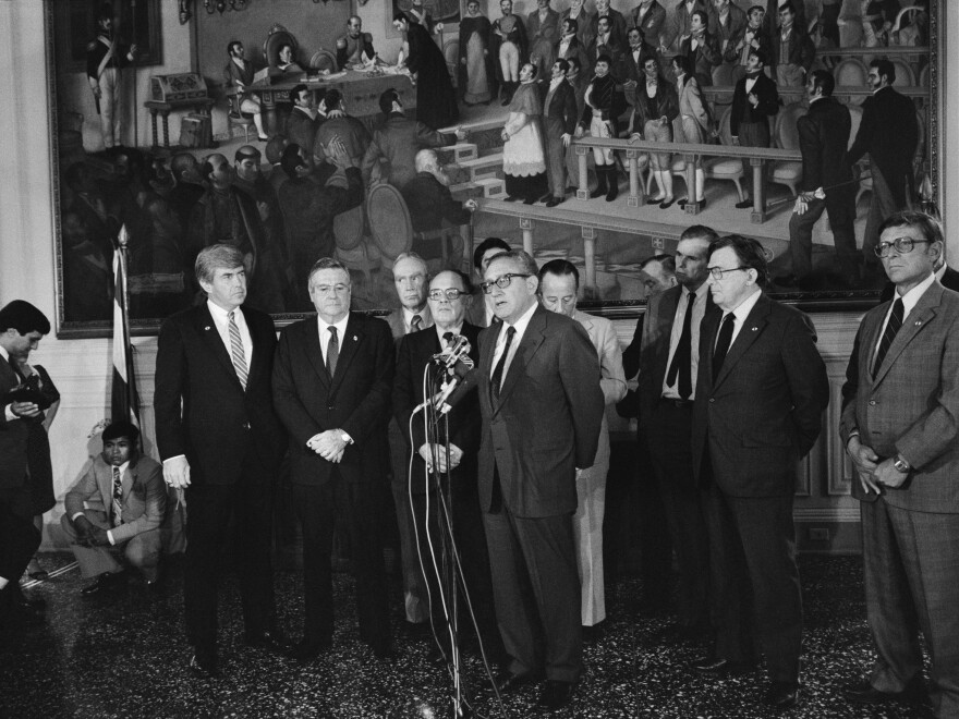 Former U.S. Secretary of State Henry Kissinger (center) speaks to the media during a joint press conference with Salvadoran President Álvaro Magaña (center left with glasses) at the presidential palace in San Salvador, El Salvador, on Oct. 13, 1983. Kissinger warned the Salvadoran government that continued support from the U.S. was dependent on improved respect for human rights.