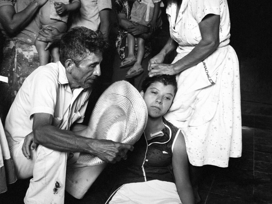 The sister of a civil defenseman (center) faints upon hearing of the death of her brother during an overnight attack on the civil defense post in Santa Clara, El Salvador, in July 1982.