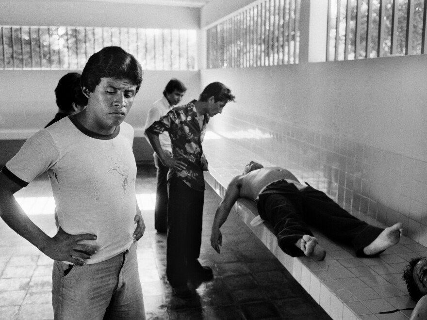 Unidentified men look at two corpses in the city morgue in La Libertad, El Salvador, on Aug. 10, 1984. Both victims were shot in the face and showed additional signs of bruising.