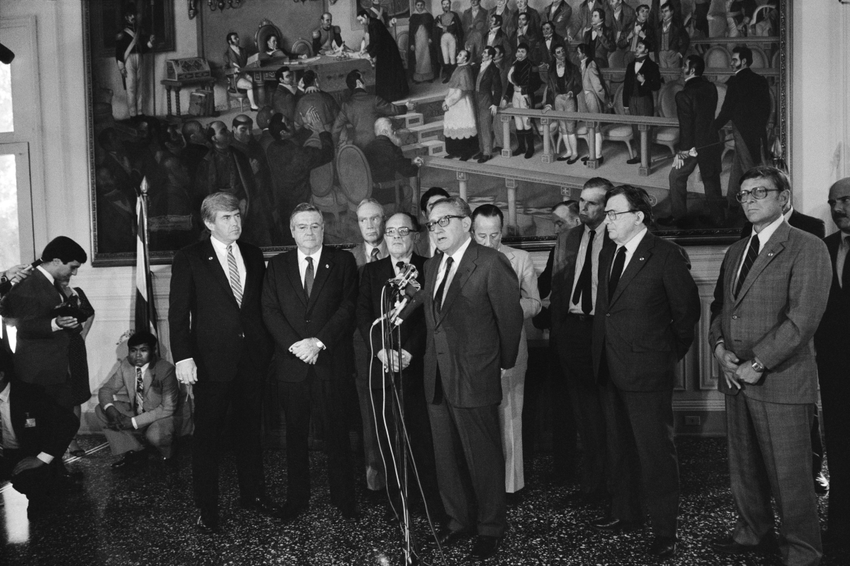 Former U.S. Secretary of State Henry Kissinger (center) speaks to the media during a joint press conference with Salvadoran President Álvaro Magaña (center left with glasses) at the presidential palace in San Salvador, El Salvador, on Oct. 13, 1983. Kissinger warned the Salvadoran government that continued support from the U.S. was dependent on improved respect for human rights.