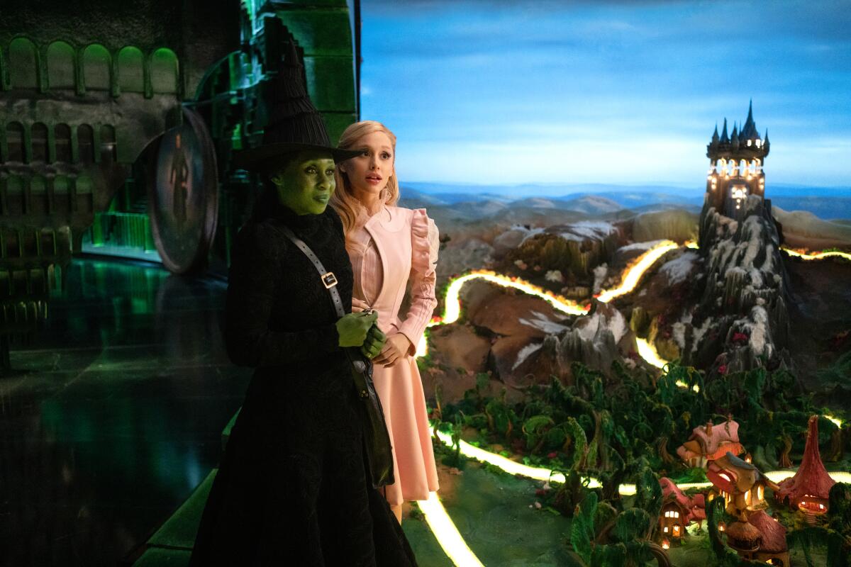 Cynthia Erivo in green makeup and witch's hat with Ariana Grande in a pink suit.